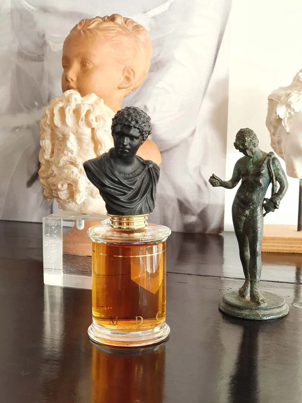Parfums MDCI bottle with dark classical bust displayed among antique sculptures