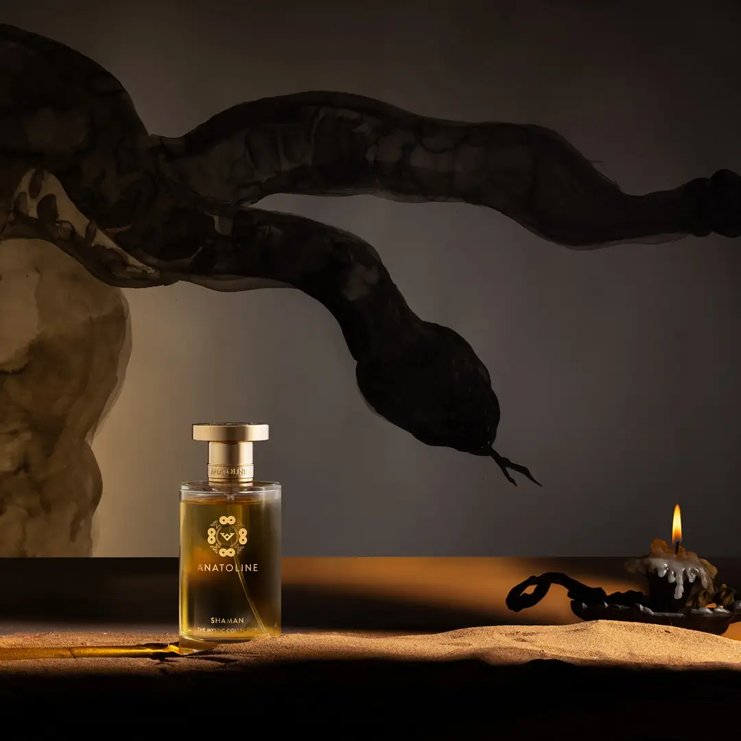 Three ANATOLINE perfume bottles displayed in dark architectural recesses above sand