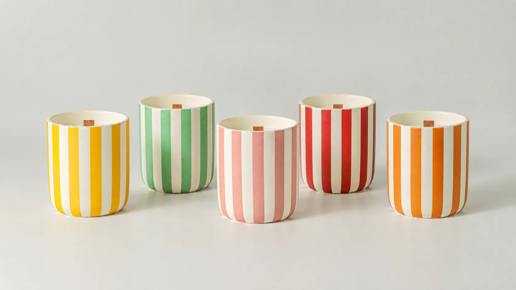 Five ceramic candle cups in yellow, green, pink, red and orange vertical stripe designs