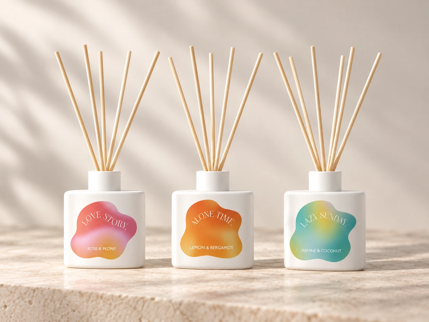 Three white reed diffuser bottles with pink, orange and blue-green gradient fragrance labels
